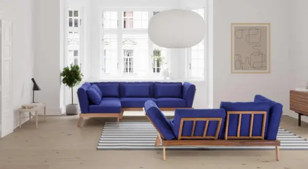 Ein tiefblaues Sofa mitten im Raum, mit Holzrahmen und passenden Kissen. Ein Streifen-Teppich liegt davor.