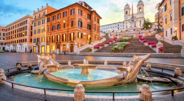 Fontana della Barcaccia e scalinata di Trinità dei Monti a Roma, con edifici storici e fiori colorati.