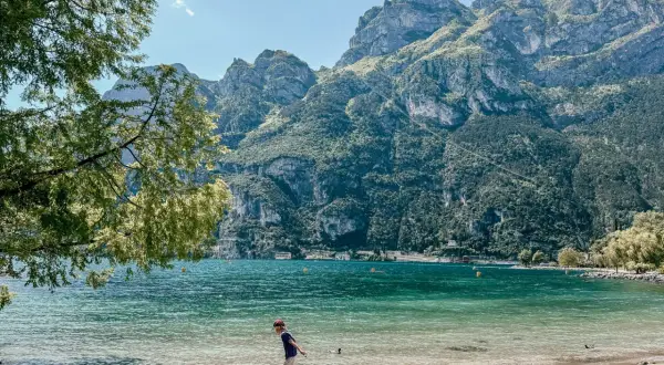 Chłopiec bawi się na plaży nad Jeziorem Garda, w tle góry. Idealne pola kempingowe czekają na odkrycie.
