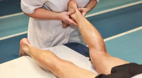 Fizjoterapeuta wykonuje masaż ścięgna Achillesa sportowca, łagodząc napięcie po treningu.