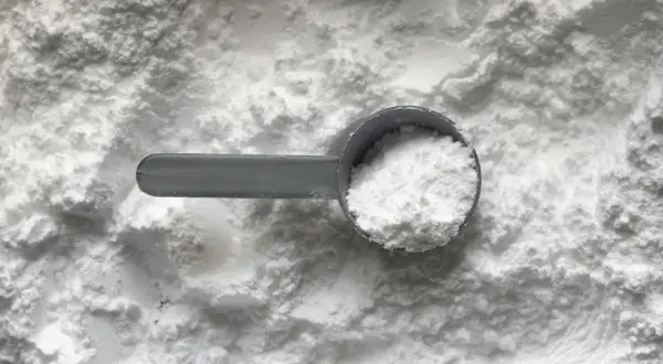 Miarka z białym proszkiem, prawdopodobnie disodium edta, na tle sypkiego materiału.