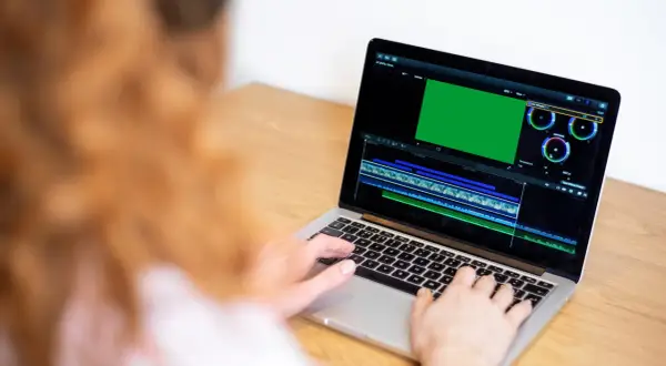 Osoba pracuje na laptopie, edytując wideo. Na ekranie widać zielony podgląd i oś czasu, co sugeruje, że uczy się, jak nagrywać ekran na laptopie.