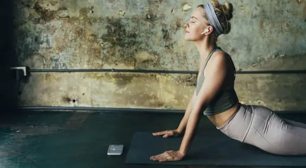 Mujer en postura de cobra, con auriculares, meditando. Considera las contraindicaciones de la postura de la cobra si tienes problemas de espalda.
