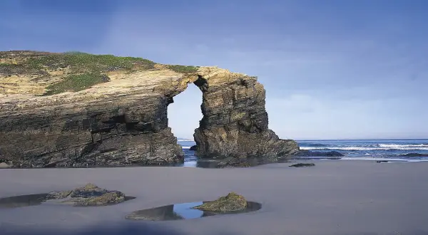 Arco natural en la costa de Ribadeo, con el mar y el cielo azul de fondo.