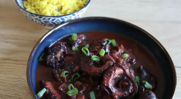 Un plat de daube de poulpe savoureux, garni de ciboule fraîche, servi avec du riz jaune parfumé.
