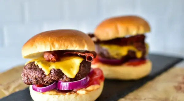 Zwei saftige Burger mit geschmolzenem Käse, knusprigem Speck und roten Zwiebelringen. Die Burger patties sind perfekt gegrillt.