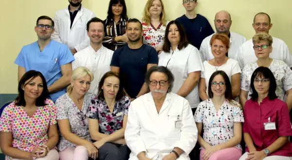 Grupa lekarzy i pielęgniarek w białych fartuchach i kolorowych strojach medycznych pozuje do zdjęcia.