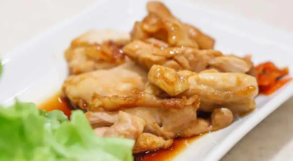 Straccetti di pollo succulenti e dorati, serviti su un piatto bianco con insalata fresca e carote sottaceto.