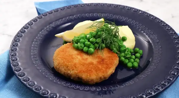 En gyllene havets wallenbergare serveras med potatis, gröna ärtor, citronklyfta och dill på en mörkblå tallrik.