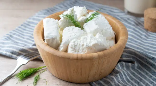 Półmisek z twarogiem półtłustym, udekorowany koperkiem. Obok widelec i szklanka mleka. Idealny na lekki posiłek, z niską zawartością kcal.