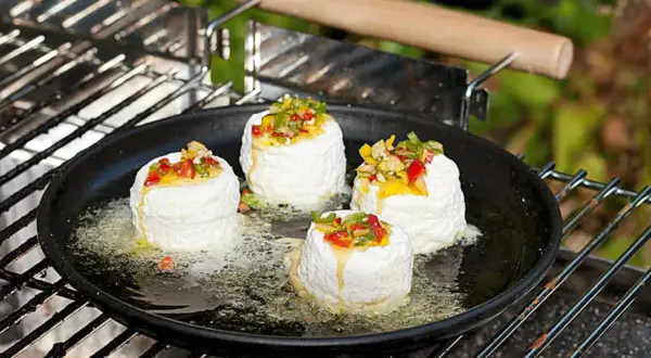 Vier runde Ziegenkäse auf einer Grillpfanne mit geschmolzenem Käse und Paprikastückchen. Perfekt für vegetarische Grillrezepte einfach.