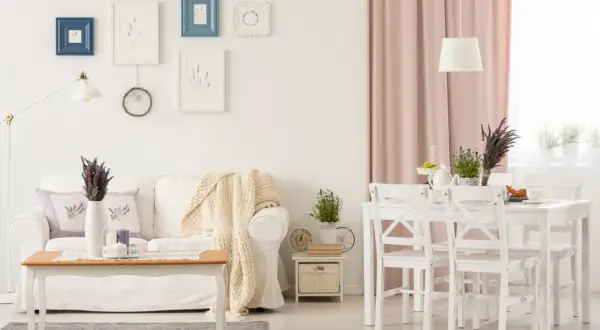 Przytulny salon w stylu shabby chic z białą kanapą, drewnianym stolikiem i pastelowymi dodatkami.