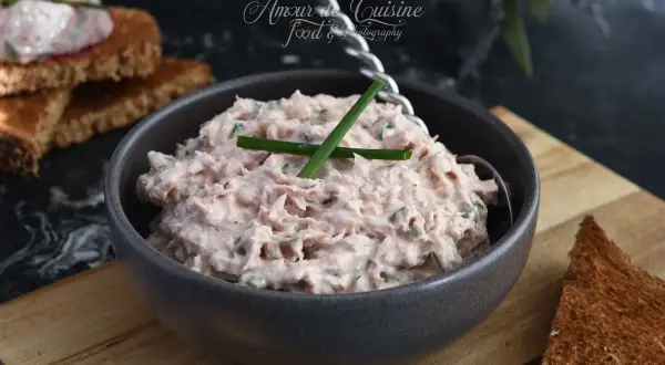 Un bol de rillettes de thon crémeuses, garnies de ciboulette, prêtes à être tartinées sur du pain grillé.