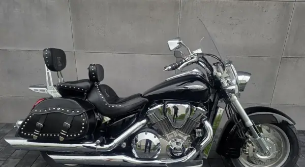 Czarny motocykl Honda VTX 1800 Neo z sakwami i oparciem dla pasażera, lśniący chromem na tle szarej ściany.
