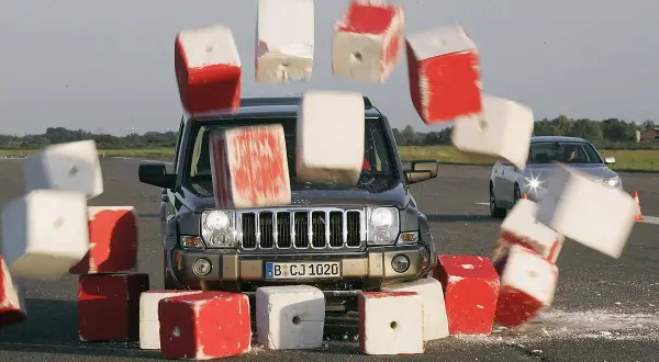 Jeep rast durch rote und weiße Blöcke, die durch die Luft fliegen. Die Szene illustriert die **Bremsweg Formel** in Aktion.