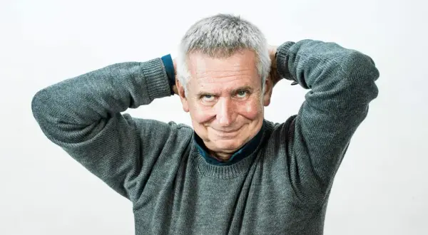 Uśmiechnięty mężczyzna z siwymi włosami, który trzyma ręce za głową. To on jest tym, kto pisze teksty żartów i anegdot, które opowiada prowadzący show.