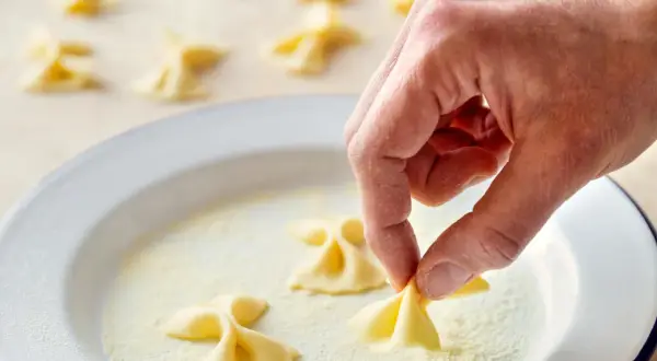 Hand formt frische Farfalle für leckere Farfalle Rezepte. Viele kleine Nudelschmetterlinge liegen bereit.