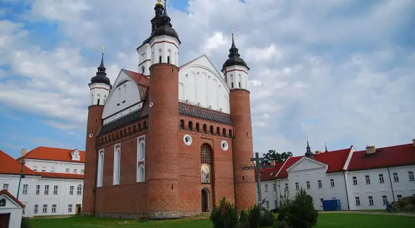 Ceglana cerkiew z kopułami i krzyżem, przypominająca o historii **unii brzeskiej**. Obok białe budynki klasztorne.