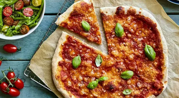 En saftig vegetarisk pizza med tomatsås och ost, toppad med färsk basilika. Bredvid en fräsch sallad med gröna bönor och körsbärstomater.