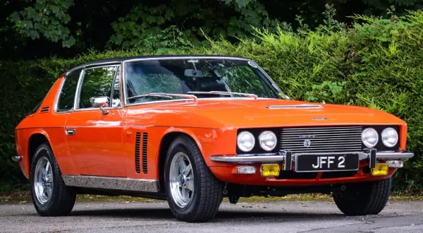 En orange Jensen Interceptor från 70-talet, en klassisk bil med en tidlös design, parkerad utomhus.