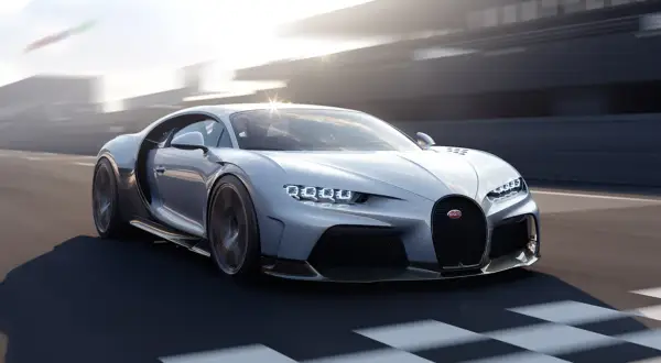 Srebrny Bugatti Chiron Super Sport pędzi po torze wyścigowym, jego światła LED błyszczą w słońcu.