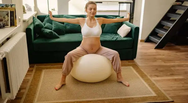 Femme enceinte faisant un exercice avec ballon pour perdre du ventre, bras écartés, yeux fermés.