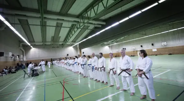 En grupp karateutövare står uppradade i en sporthall. Flera bär ett brunt bälte karate, vilket indikerar erfarenhet.