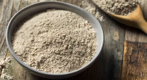Un bol de farine complète, un équivalent de farine 00 pour des recettes rustiques. Une cuillère en bois en arrière-plan.