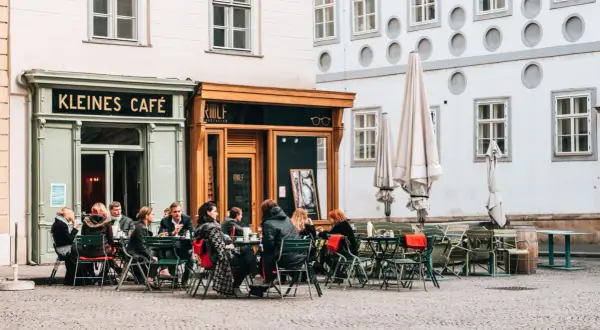 Menschen sitzen vor dem "Kleines Café" und genießen einen kleinen braunen Kaffee.