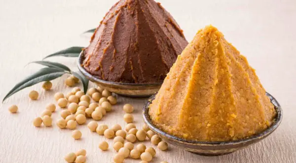 Due ciotole con miso, uno scuro e uno chiaro, circondate da fagioli di soia. Il miso è una pasta fermentata giapponese.