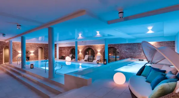 Relaks w nowoczesnym spa niedaleko Warszawy. Basen z niebieskim podświetleniem, ceglane ściany i wygodne leżaki tworzą atmosferę spokoju.