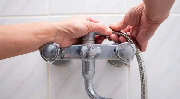 Hands working to fix a shower faucet, detaching the shower hose.