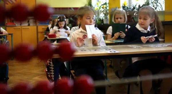 Dzieci siedzą w ławkach, ucząc się, kiedy idą do szkoły. Jedna dziewczynka trzyma kartę z cyfrą.
