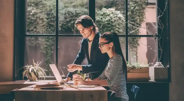 Mężczyzna wskazuje na ekran laptopa, omawiając z kobietą zadania. To dobra opinia o praktykancie, który szybko się uczy.