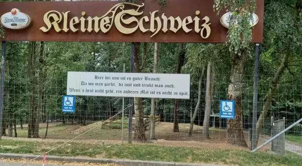 Schild "Kleine Schweiz" in Velbert. Ein Spruch lädt zum Verweilen ein. Parken, essen, trinken – perfekt für eine Wanderung.