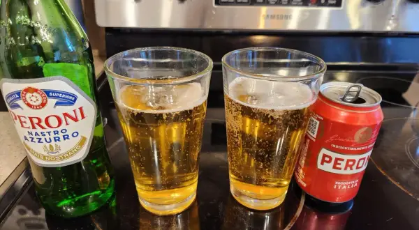 Butelka i puszka Peroni Nastro Azzurro obok dwóch szklanek piwa.