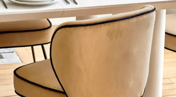 Chaises au revêtement velours couleur camel, bordées d'un passepoil noir, autour d'une table blanche.