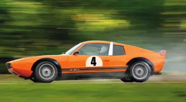 En orange Saab Sonett IV med nummer 4 på sidan susar fram på en bana, omgiven av suddiga gröna träd.