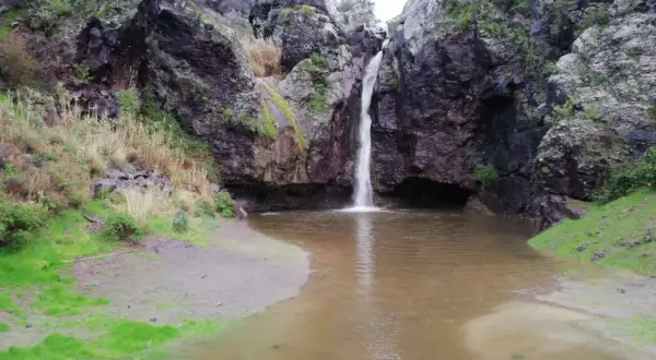 Cascada cayendo en el **charco de la paloma**, rodeado de rocas oscuras y vegetación.