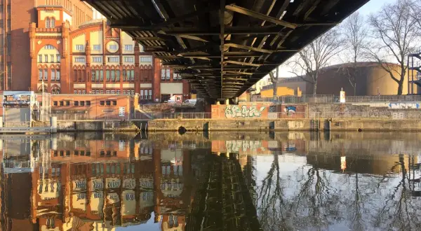 Pod mostem w Berlinie odbija się w rzece ceglana architektura i nagie drzewa.