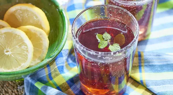 Un verre de jus de bissap pétillant, garni de menthe fraîche, à côté d'un bol de citrons tranchés. Parfait pour une journée ensoleillée.
