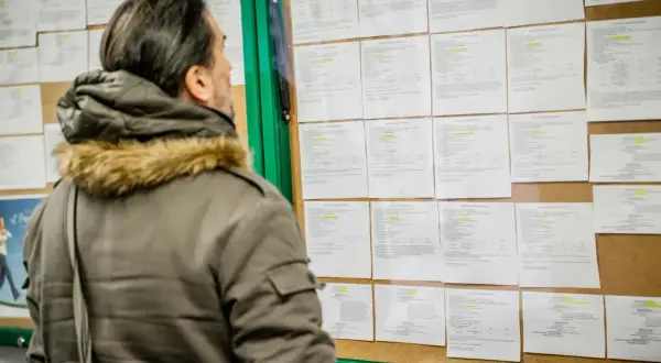 Mężczyzna w zimowej kurtce analizuje ogłoszenia na tablicy, szukając informacji o umowie zlecenie i składkach.