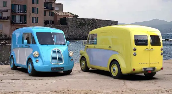 Två färgglada Morris bil-modeller, en blå och en gul, står vid havet.