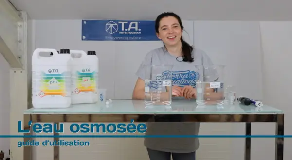 Une femme souriante présente des produits pour ajuster le pH de l'eau osmosée, avec des béchers et des bouteilles sur une table.