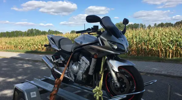 Srebrny motocykl Yamaha na przyczepce, na tle pola kukurydzy i błękitnego nieba z chmurami.