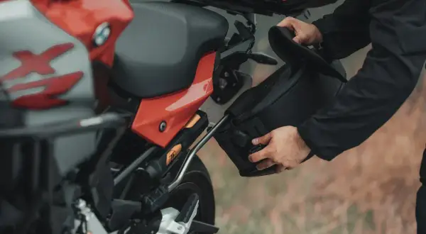 Mężczyzna montuje czarną sakwę motocyklową do czerwonego motocykla.