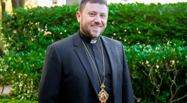 Uśmiechnięty mężczyzna w czarnym garniturze i z krzyżem na szyi, być może najmłodszy kardynał.