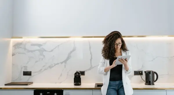 Donna con tablet in cucina moderna, valuta quanto costa rifare una cucina con finiture in marmo e illuminazione a led.