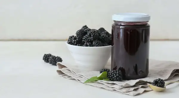 Frische Brombeeren und ein Glas selbstgemachtes Brombeergelee. So lässt sich das Gelee noch verfeinern.
