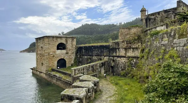 El castillo San Felipe en Ferrol, una fortaleza de piedra junto al mar, con vegetación cubriendo sus muros y un camino empedrado.